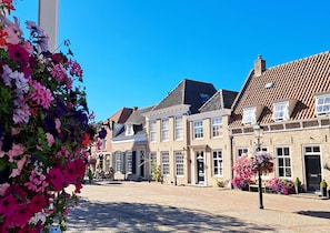 Een straat met kinderkopjes, omzoomd door traditionele bakstenen gebouwen, waarvan sommigen ramen en deuren hebben, en een heldere blauwe lucht erboven.