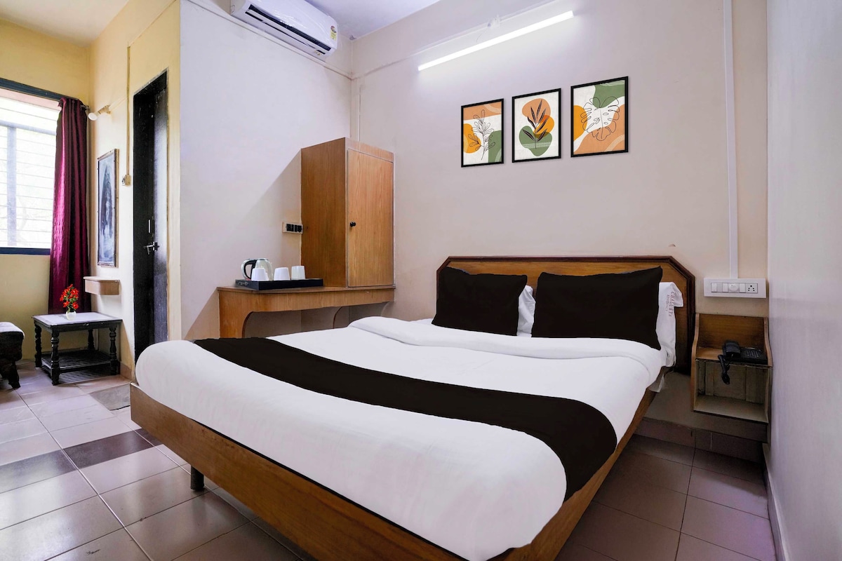 A hotel room with a bed, a wooden wardrobe, a small table with a kettle, and a wall-mounted phone.