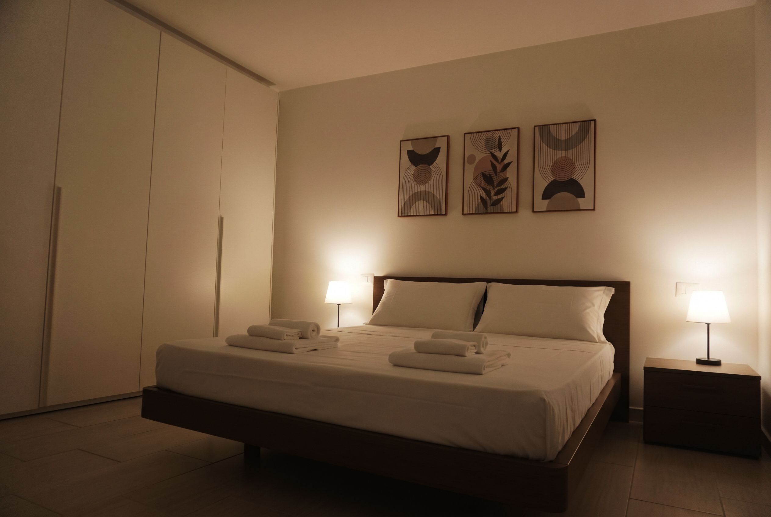 Una habitación de hotel con una cama, dos lámparas de noche y tres obras de arte en la pared.