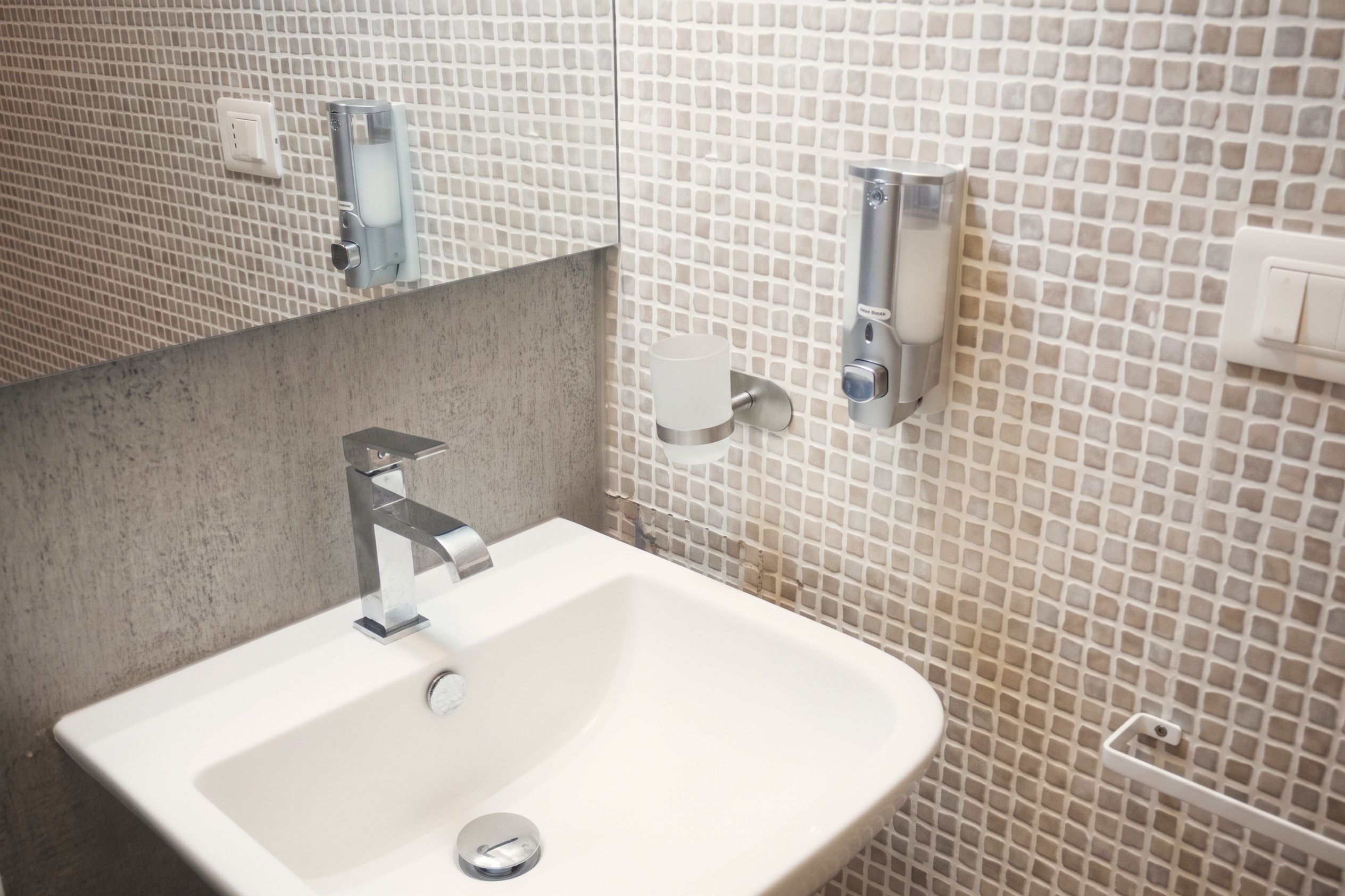 A bathroom with a white sink, a mirror, and a tiled wall.
