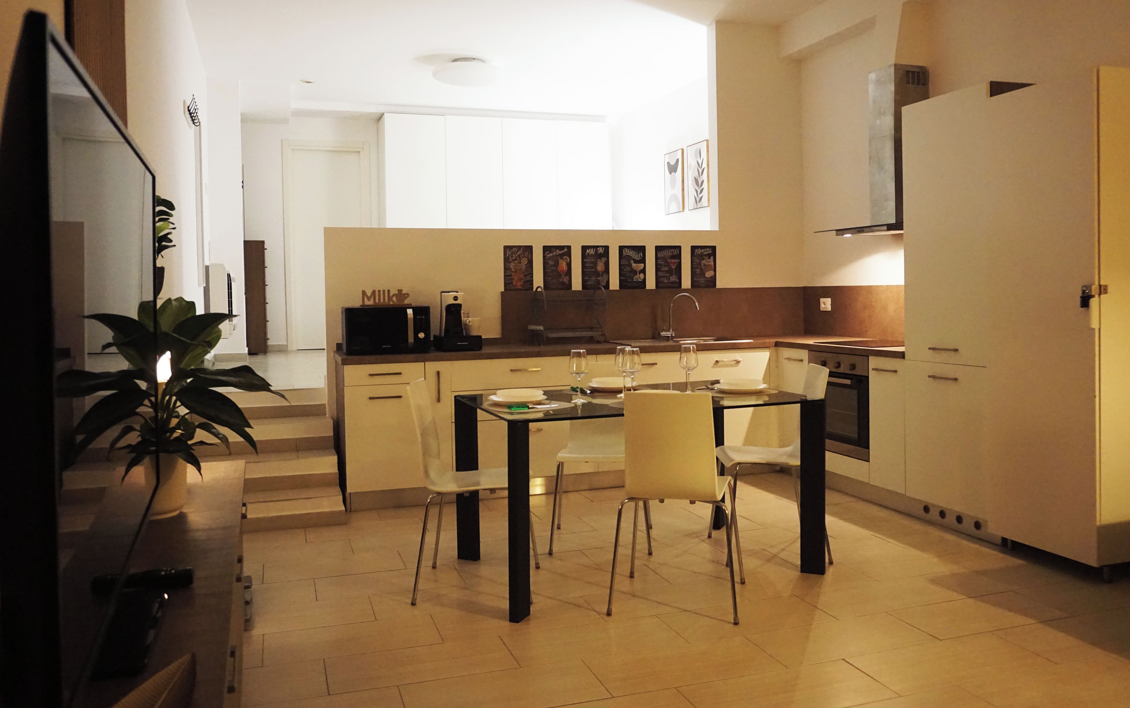 Una cocina moderna con comedor, que cuenta con un televisor de pantalla plana, cafetera y microondas.