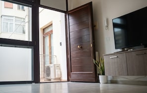 Habitació amb porta corredissa de vidre que dona a un balcó, televisió de pantalla plana penjada a la paret i una planta en test.
