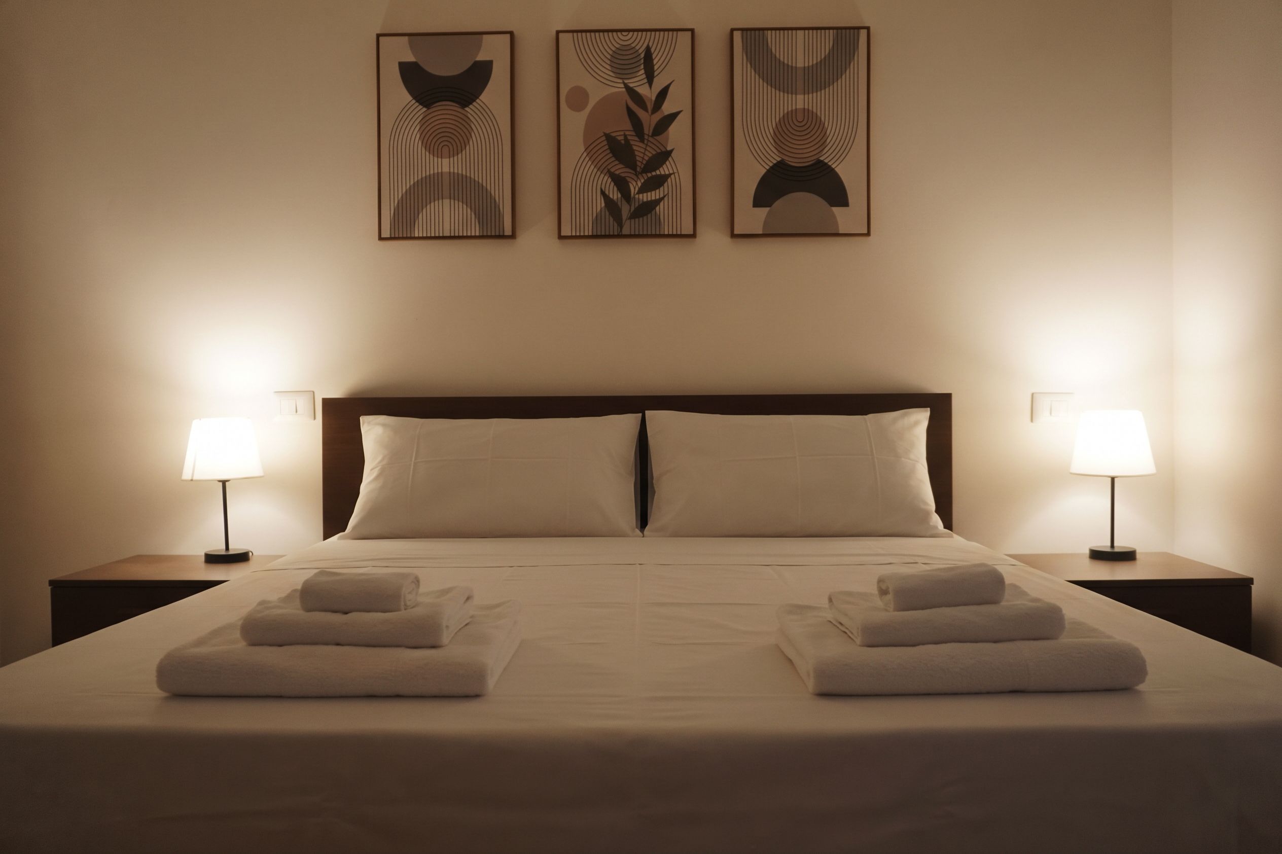 A hotel room with a large bed, two bedside lamps, and three wall-mounted artworks.