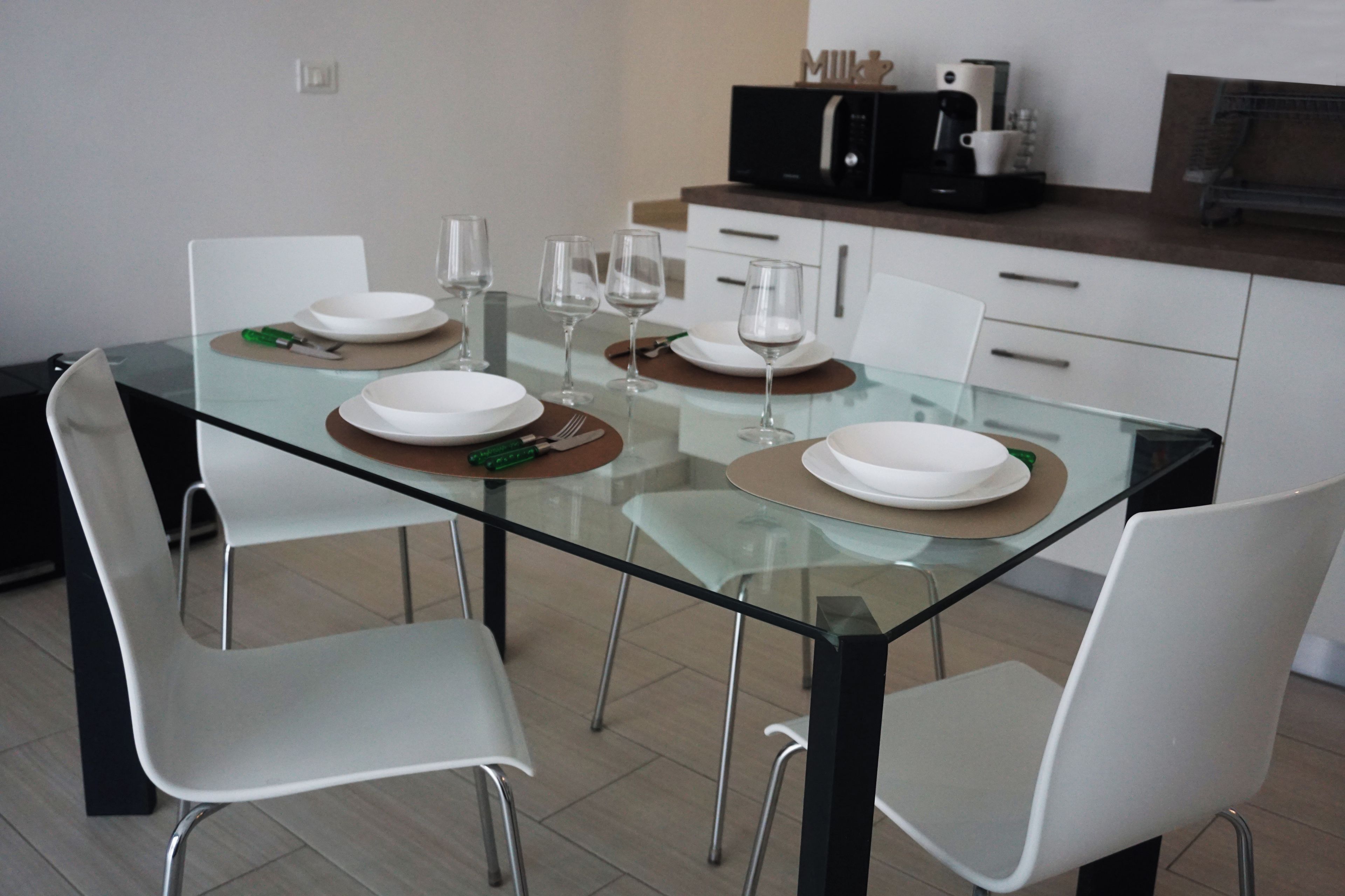 Una cocina moderna con una mesa de vidrio, sillas blancas y una cafetera.