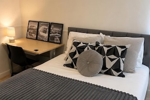 Habitación de hotel con cama, escritorio, silla y lámpara. En la pared hay tres cuadros enmarcados.