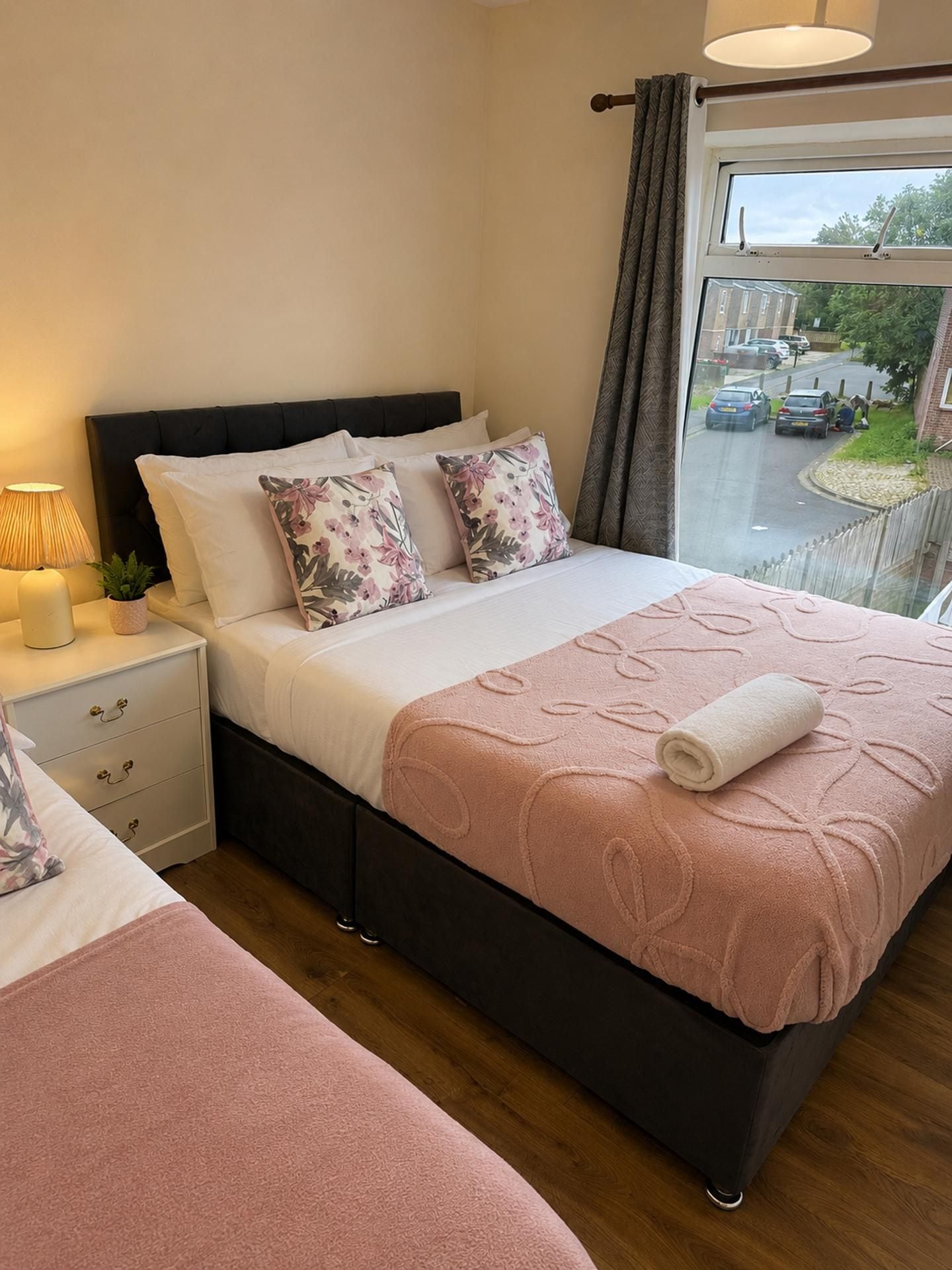 A bedroom with a bed, bedside tables, a window with a view of the street, and a nightstand with a lamp.