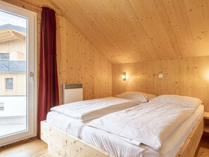 A wooden room with a bed, a window with curtains, and a radiator. - One-bedroom Cabin (Sankt Georgen am Kreischberg)