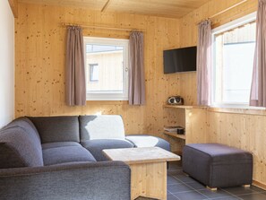 A cozy room with a sofa, a small table, and a television mounted on the wall. - One-bedroom Cabin (Sankt Georgen am Kreischberg)