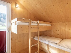 Llits superposats en una habitació de fusta, amb una porta i un lluminari.