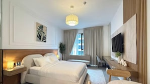A hotel room with a bed, bedside table, lamp, TV, and a seating area with a table and chairs. - Maison Sahab - Stylish Studio in Tiraz Building (Sharjah)