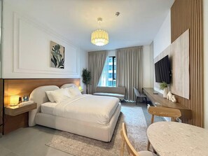 Una camera d'albergo con un letto, un comodino, una lampada, una TV e un'area salotto con tavolo e sedie.