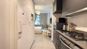 A modern kitchen with a microwave, stove, and oven. There is a dining area with a table and chairs. - Maison Sahab - Stylish Studio in Tiraz Building (Sharjah)