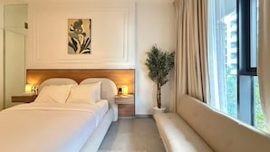 A hotel room with a large bed, bedside tables, a potted plant, and a view of the outside. - Maison Sahab - Stylish Studio in Tiraz Building (Sharjah)