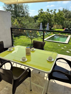 An outdoor patio with a table set for two, surrounded by chairs, a small pool, and a view of a lush garden. - Le cocon de Caumont (Caumont-sur-Durance)