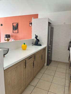 A kitchen with a white countertop, wooden cabinets, a yellow bowl, a black kettle, and a framed leaf artwork on the wall. - Le cocon de Caumont (Caumont-sur-Durance)