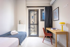 Ein Schlafzimmer mit einem Bett, einem Schreibtisch mit Stuhl, einem Fenster und einem gerahmten Bild an der Wand.