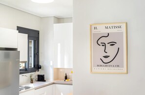 A modern kitchen with white cabinetry, a black-framed window, and a framed artwork on the wall. - FiftySeven Athens - Two Ways Outside, 2BR | 302 (Athina)