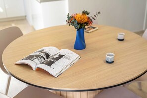 A round wooden table with a book, a blue vase with flowers, and a small white mug. - FiftySeven Athens - Two Ways Outside, 2BR | 302 (Athina)