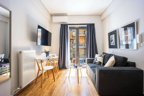 Ein modernes Wohnzimmer mit einer Couch, einem Esstisch mit Stühlen, einem an der Wand befestigten Fernseher und Blick auf einen Balkon.