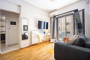 Ein modernes Wohnzimmer mit einer Couch, einem Esstisch mit Stühlen, einem an der Wand befestigten Fernseher und einer Glastür zum Außenbalkon.