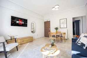 A modern living room with a flat-screen TV, a dining area with a table and chairs, a sofa, and a coffee table with magazines. - FiftySeven Athens - 2BR, Terrace & Balcony | 301 (Athina)