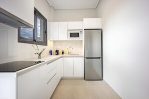 A modern kitchen with white cabinetry, a stainless steel refrigerator, a microwave, and a black countertop. - FiftySeven Athens - 2BR, Terrace & Balcony | 301 (Athina)