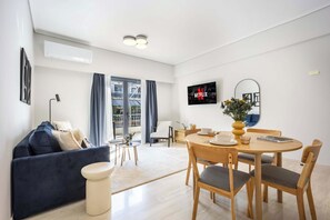 A modern living room with a sofa, a dining table set for four, and a television mounted on the wall. - FiftySeven Athens - 2BR, Terrace & Balcony | 301 (Athina)