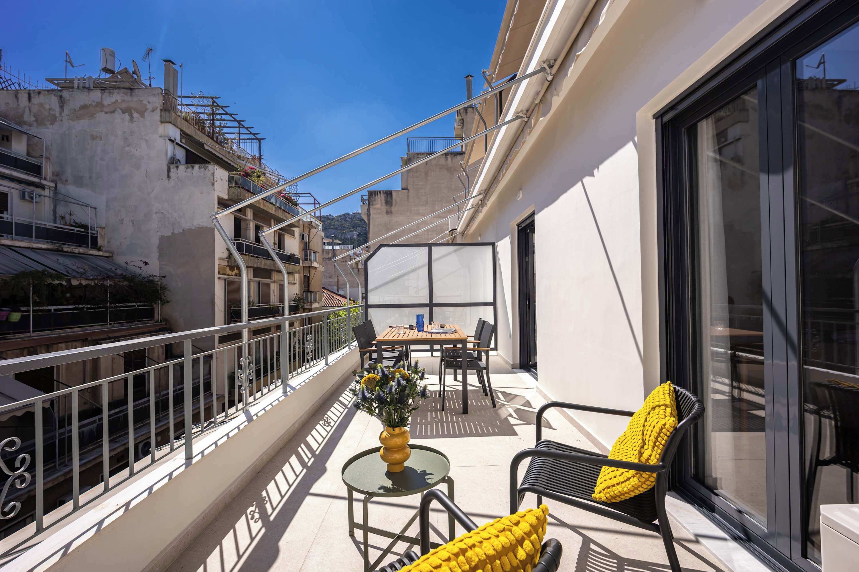 Un balcon avec une table et des chaises, un pot de fleurs et une vue sur le paysage urbain.