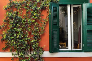 Ein Fenster mit grünen Fensterläden, das teilweise geöffnet ist und einen Blick ins Zimmerinnere auf Tisch und Stühle gewährt.
