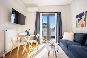 Ein modernes Wohnzimmer mit einer Couch, einem an der Wand montierten Fernseher, einem Essbereich mit Stühlen und einem Tisch und Blick durch die offene Tür.