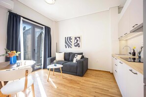Un saló modern amb un sofà gris, una taula rodona petita i una zona de cuina amb armaris blancs i un taulell de fusta.