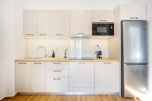 A modern kitchen with white cabinets, a stainless steel refrigerator, a Bosch microwave, and a coffee machine. - FiftySeven Athens - Local Ease, Balcony | 101 (Athina)