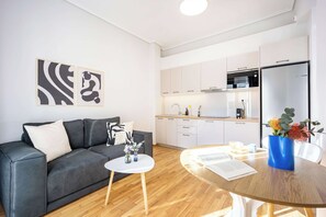Un apartament modern amb un sofà gris, una taula petita blanca i una cuina amb un frigorífic Bosch.
