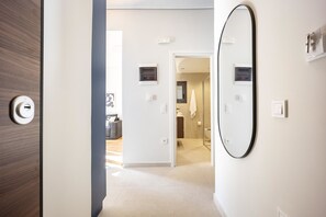 A hallway leading to a bathroom with a large mirror, a door with a keyhole, and a light switch on the wall. - FiftySeven Athens - Local Ease, Balcony | 101 (Athina)