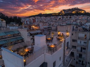 A rooftop terrace with outdoor seating and a view of a cityscape at sunset. - FiftySeven Athens - Local Ease, Balcony | 101 (Athina)