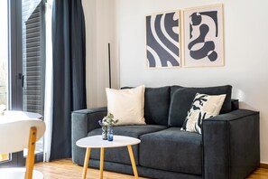 A modern living room with a grey sofa, a small round table, and two abstract wall art pieces. - FiftySeven Athens - Local Ease, Balcony | 101 (Athina)