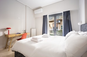 A hotel room with a bed, a desk with a lamp, a chair, and a window with curtains. - FiftySeven Athens - Spacious 2BR, Terrace | 103 (Athina)