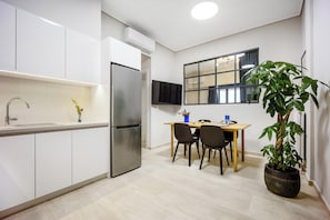 A compact kitchen with a built-in refrigerator, a dining area with a table and chairs, and a potted plant. - FiftySeven Athens - Terrace Days, 2BR | 102 (Athina)