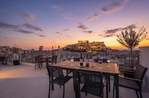 A rooftop terrace with a table set for dining, overlooking a historic cityscape and a prominent ancient fortress. - FiftySeven Athens - Terrace Days, 2BR | 102 (Athina)