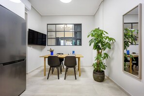 A compact kitchen with a built-in refrigerator, a dining table with chairs, a window with curtains, and a large potted plant. - FiftySeven Athens - Terrace Days, 2BR | 102 (Athina)