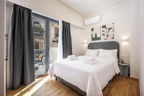 A hotel room with a bed, a nightstand, a wall-mounted air conditioner, and a view through a sliding glass door. - FiftySeven Athens - Towards Lycabettus | 203 (Athina)