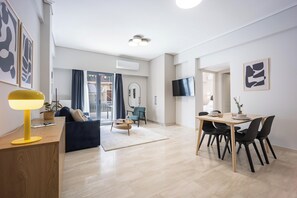 A modern living room with a sofa, coffee table, and dining area with chairs. - FiftySeven Athens - Towards Lycabettus | 203 (Athina)