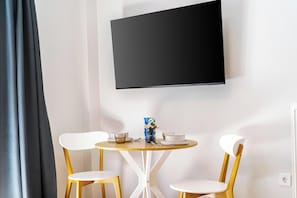 A room with a round wooden table, two white chairs, a small vase with flowers, and a flat-screen TV mounted on the wall. - FiftySeven Athens - Off the Street, Balcony | 204 (Athina)
