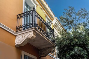 A building corner with a balcony featuring ornate black wrought iron railings and a white decorative cornice. - FiftySeven Athens - Off the Street, Balcony | 204 (Athina)