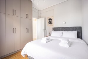 Ett modernt sovrum med en stor säng, vita sängkläder, en grå sänggavel och en minimalistisk design.