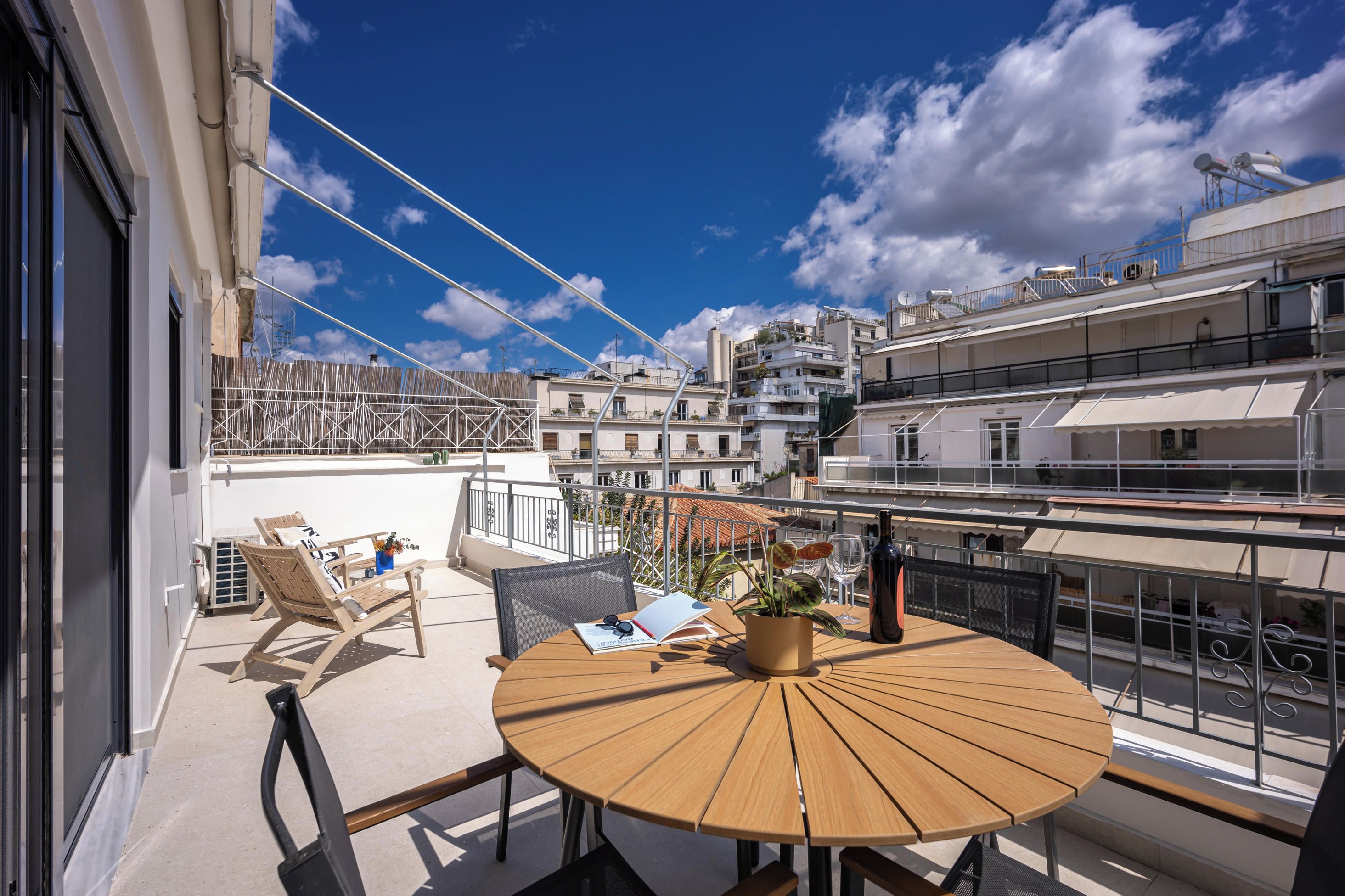 Une table ronde en bois, entourée de chaises, sur un balcon donnant sur une vue panoramique de la ville.