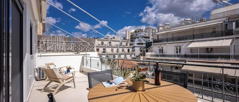 A round wooden table with chairs on a balcony overlooking a cityscape.