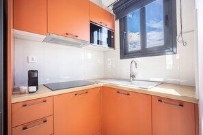 A compact kitchen with orange cabinetry, a Bosch microwave, a sink, and a window with a view of the sky. - FiftySeven Athens - Acropolis View Terrace | 501 (Athina)