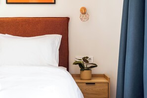 A neatly made bed with white linens, a wooden nightstand with a potted plant, and a wall-mounted light fixture. - FiftySeven Athens - Acropolis View Terrace | 501 (Athina)