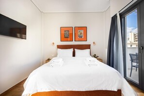 A hotel room with a large bed, two framed pictures on the wall, a TV mounted on the wall, and a view of the outside through a sliding door. - FiftySeven Athens - Acropolis View Terrace | 501 (Athina)